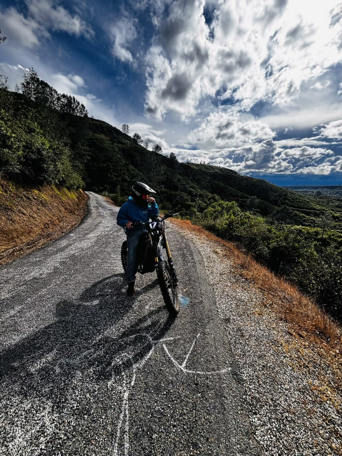 Carter on his dirt bike on a scenic mountain road beneath a dramatic sky